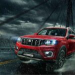 Red Mahindra Scorpio-N with ADAS features driving in heavy rain on a bridge