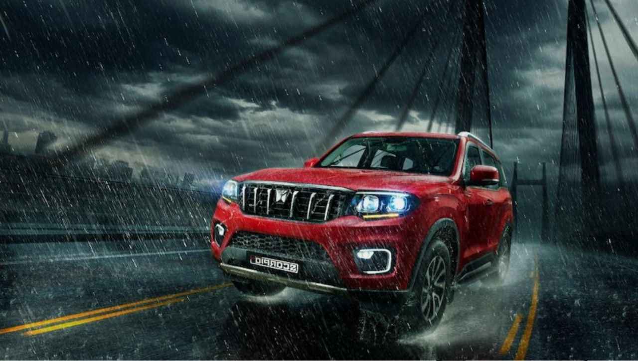 Red Mahindra Scorpio-N with ADAS features driving in heavy rain on a bridge